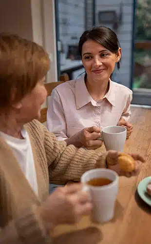 Photo d'une aide à domicile partageant un moment de complicité avec une personne âgée dans un intérieur lumineux.